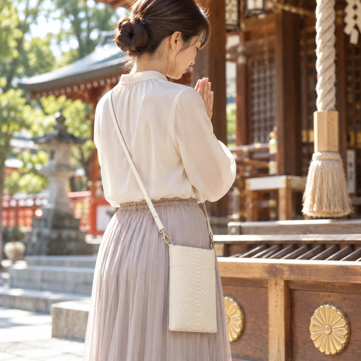 白蛇革のポーチを斜めがけして、社殿の前で手を合わせる女性